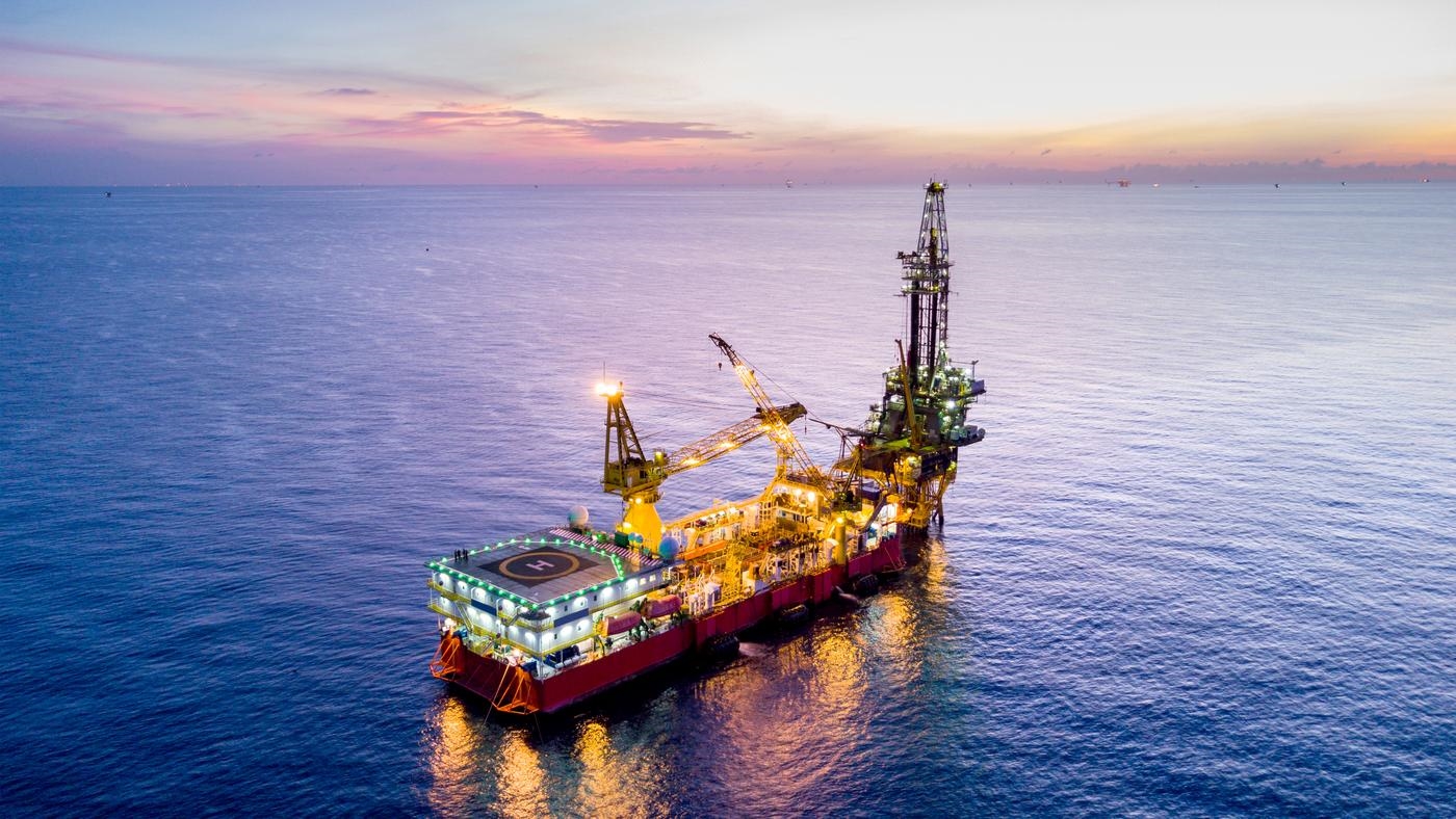 An aerial view of an oil rig in the ocean at sunset, with other rigs in the distance.