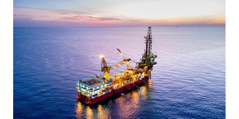 An aerial view of an oil rig in the ocean at sunset, with other rigs in the distance.