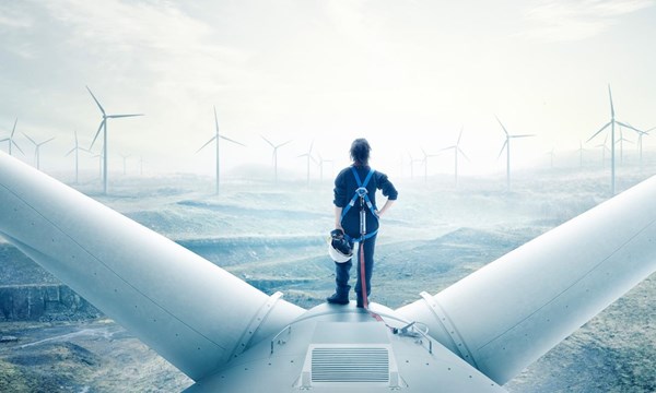 A person standing on top of a wind turbine, looking out at an wind farm, covered in fog.