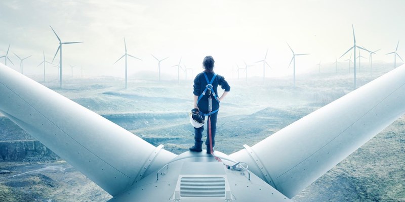 A person standing on top of a wind turbine, looking out at an wind farm, covered in fog.