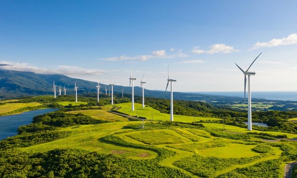 A row of wind turbines in the mountain coastal cliffs, under the blue sky.