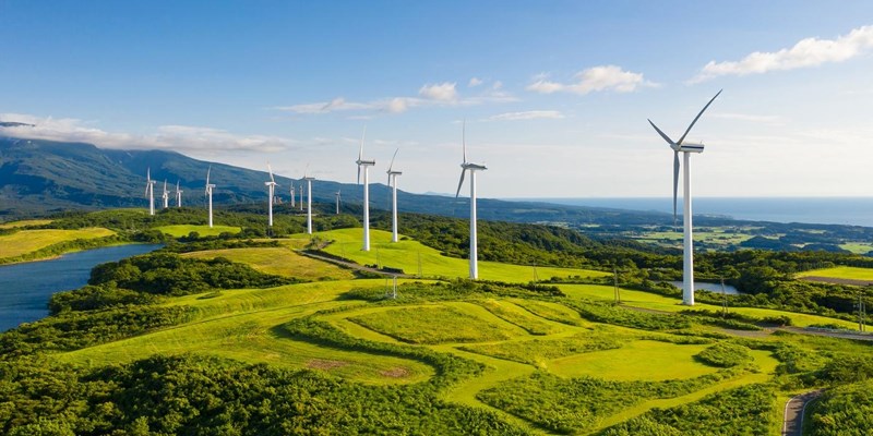 A row of wind turbines in the mountain coastal cliffs, under the blue sky.