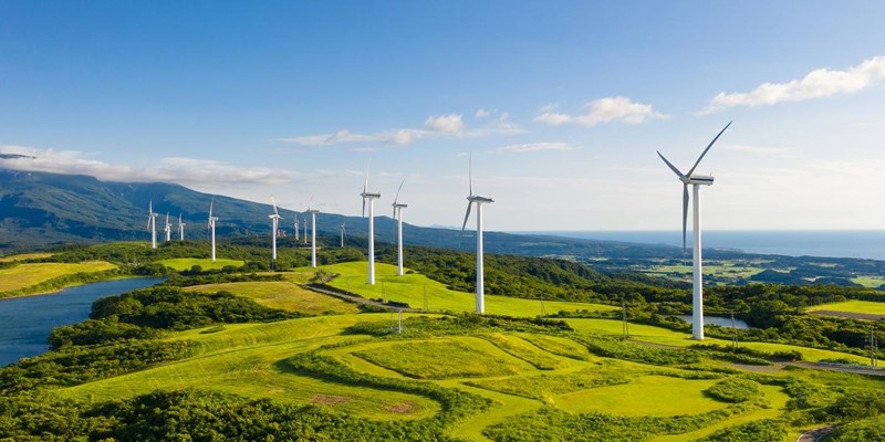 A row of wind turbines in the mountain coastal cliffs, under the blue sky.