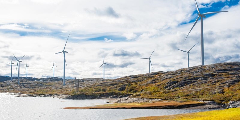 Wind turbines across rocky hills, next to a lake.