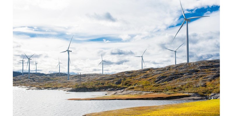 Wind turbines across rocky hills, next to a lake.