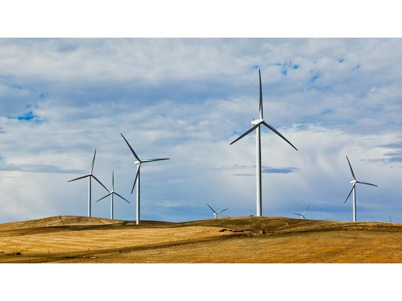 A group of wind turbines in a crop field, under a cloudy blue sky.