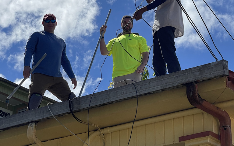 Image shows three people installing power cables on the roof of a house